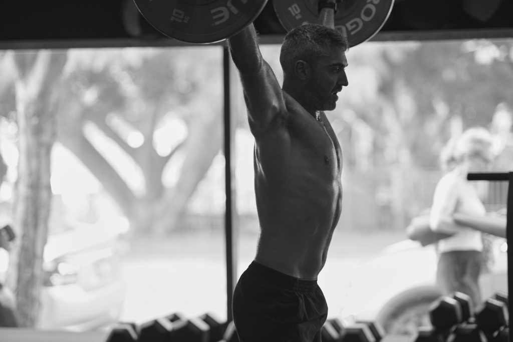 Male athlete performing an overhead barbell press at CrossFit Bondi gym, demonstrating strength training for energy and longevity.