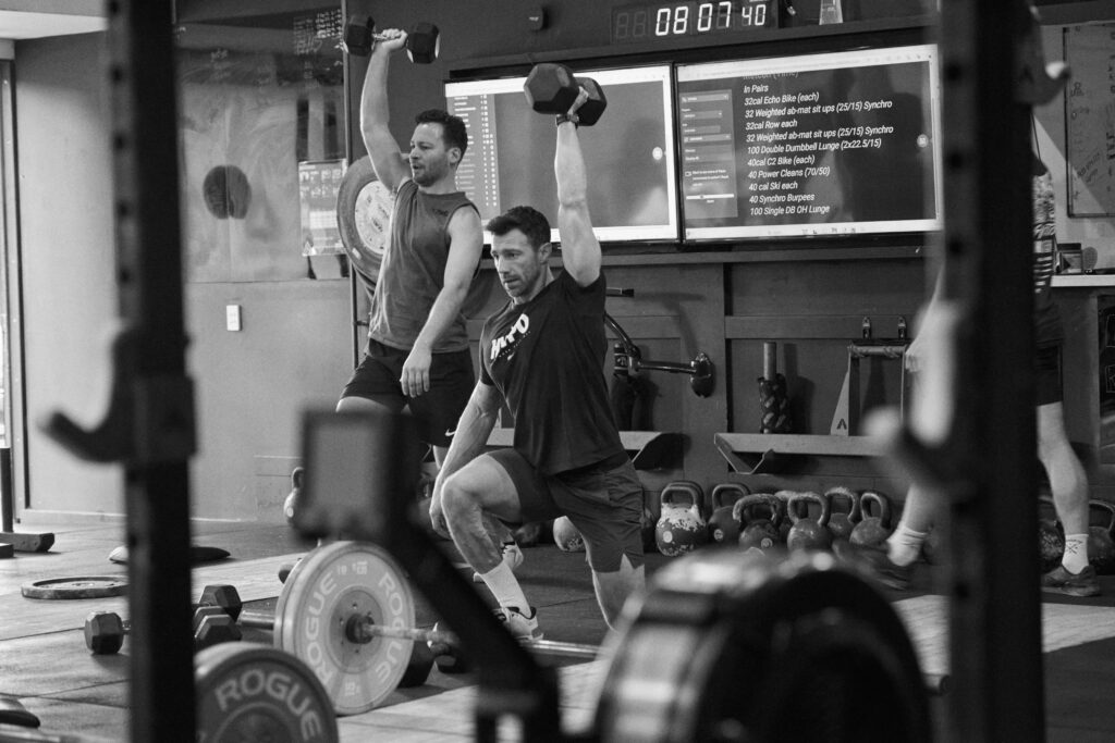 CrossFit Bondi athlete performing an overhead dumbbell movement while learning proper breathing and bracing technique during strength training in Sydney.